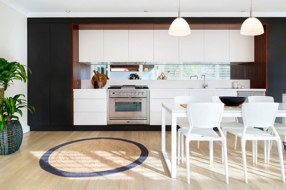 Photo of a mid-sized beach style galley kitchen in Sydney with flat-panel cabinets and light hardwood floors.