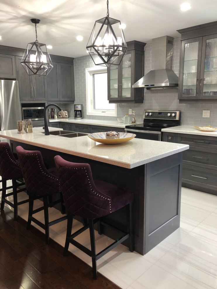 This is an example of a modern eat-in kitchen in Toronto with a farmhouse sink, shaker cabinets, grey cabinets, quartz benchtops, grey splashback, glass tile splashback, stainless steel appliances, porcelain floors, white floor and white benchtop.