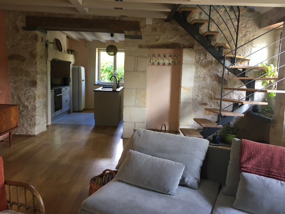 Mittelgroßes Country Wohnzimmer mit rosa Wandfarbe, hellem Holzboden, Kamin, Kaminumrandung aus Stein, beigem Boden, freigelegten Dachbalken und Steinwänden in Angers