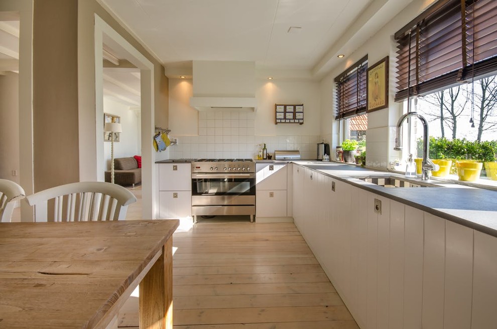 Design ideas for a mid-sized transitional l-shaped kitchen in Devon with white cabinets, with island, an undermount sink, beaded inset cabinets, white splashback, ceramic splashback, stainless steel appliances, light hardwood floors, beige floor and grey benchtop.