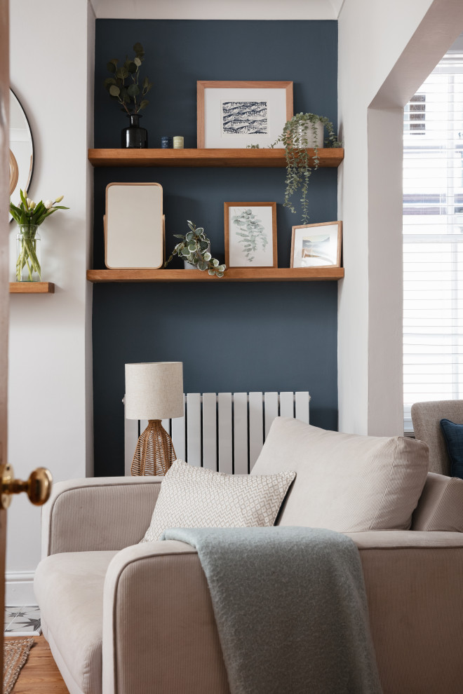 コーンウォールにある高級な中くらいな北欧スタイルのおしゃれなリビング (青い壁、無垢フローリング、標準型暖炉、漆喰の暖炉まわり、コーナー型テレビ、茶色い床、アクセントウォール) の写真