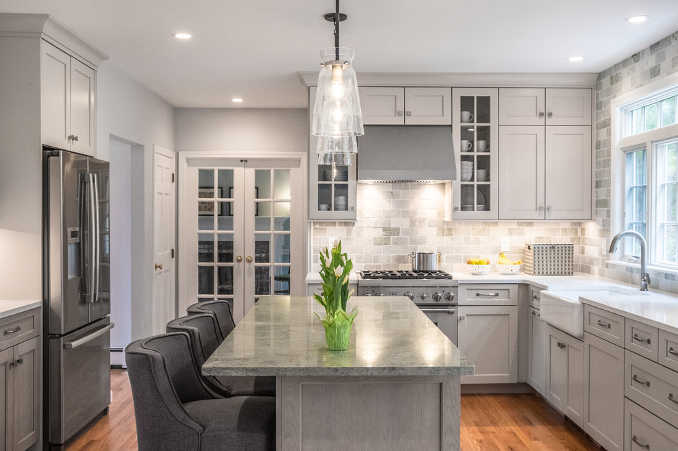 Design ideas for a mid-sized transitional u-shaped kitchen in Boston with a farmhouse sink, shaker cabinets, grey cabinets, grey splashback, stainless steel appliances, medium hardwood floors, with island, brown floor and white benchtop.