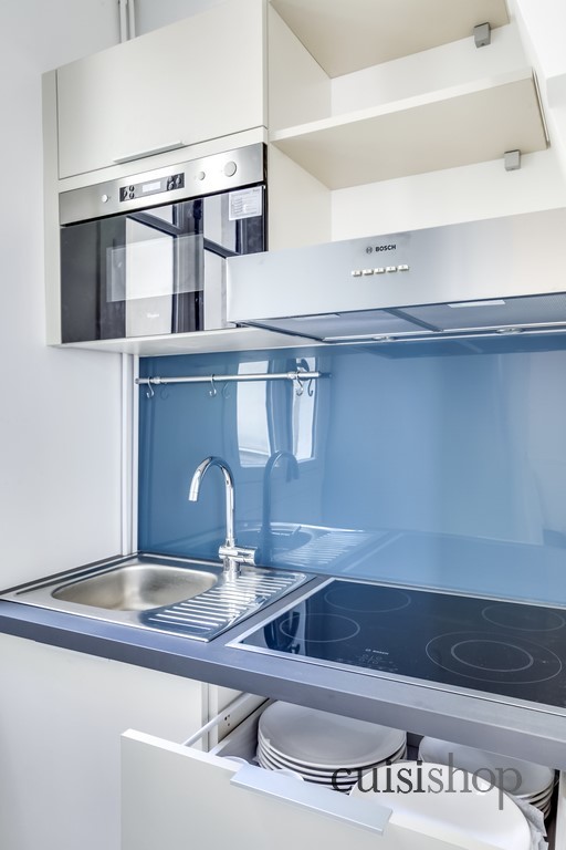 Small contemporary l-shaped open plan kitchen in Paris with laminate benchtops, with island, a single-bowl sink, flat-panel cabinets, beige cabinets, blue splashback, glass sheet splashback, stainless steel appliances, light hardwood floors, brown floor and grey benchtop.