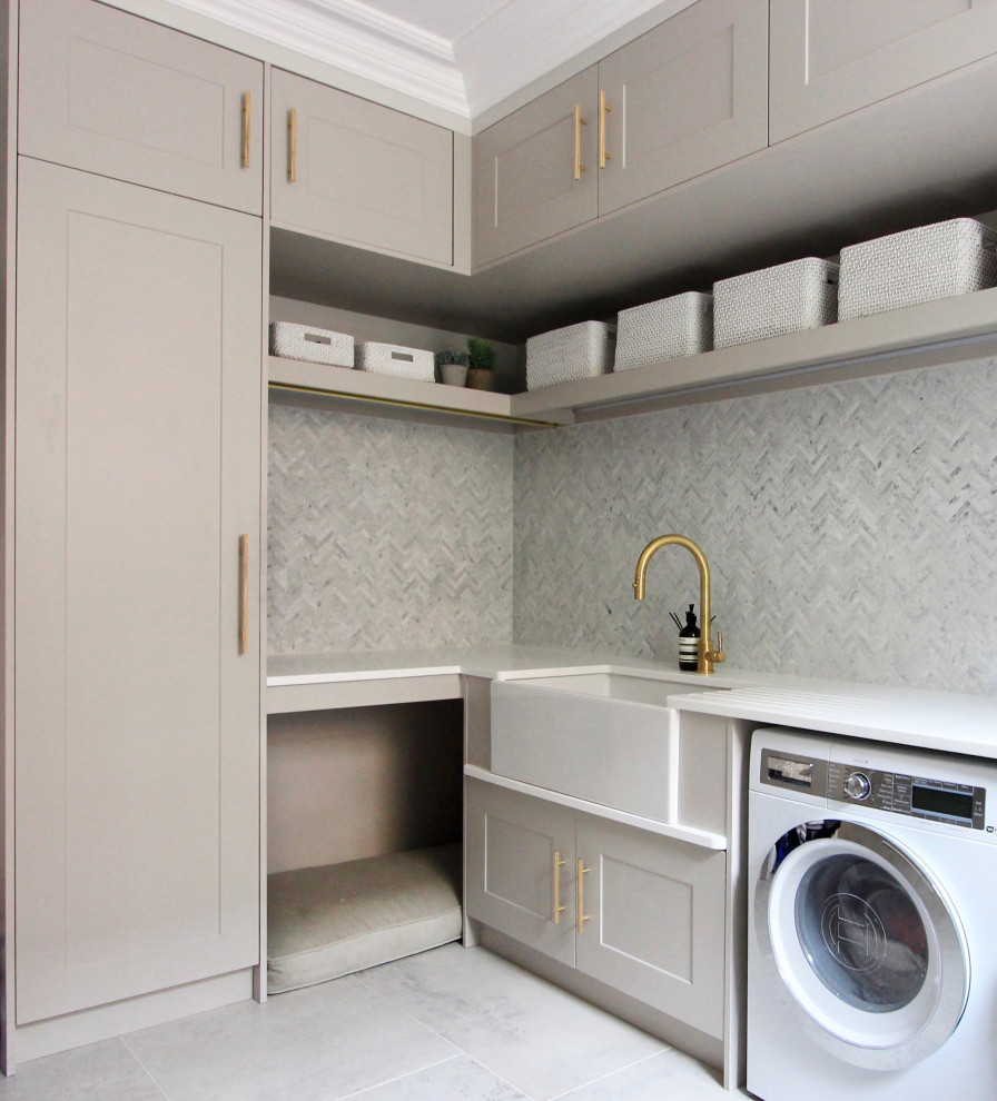 Modern inredning av en stor vita vitt liten tvättstuga, med en rustik diskho, skåp i shakerstil, grå skåp, bänkskiva i kvartsit, grått stänkskydd, stänkskydd i marmor, vita väggar, en tvättmaskin och torktumlare bredvid varandra och grått golv