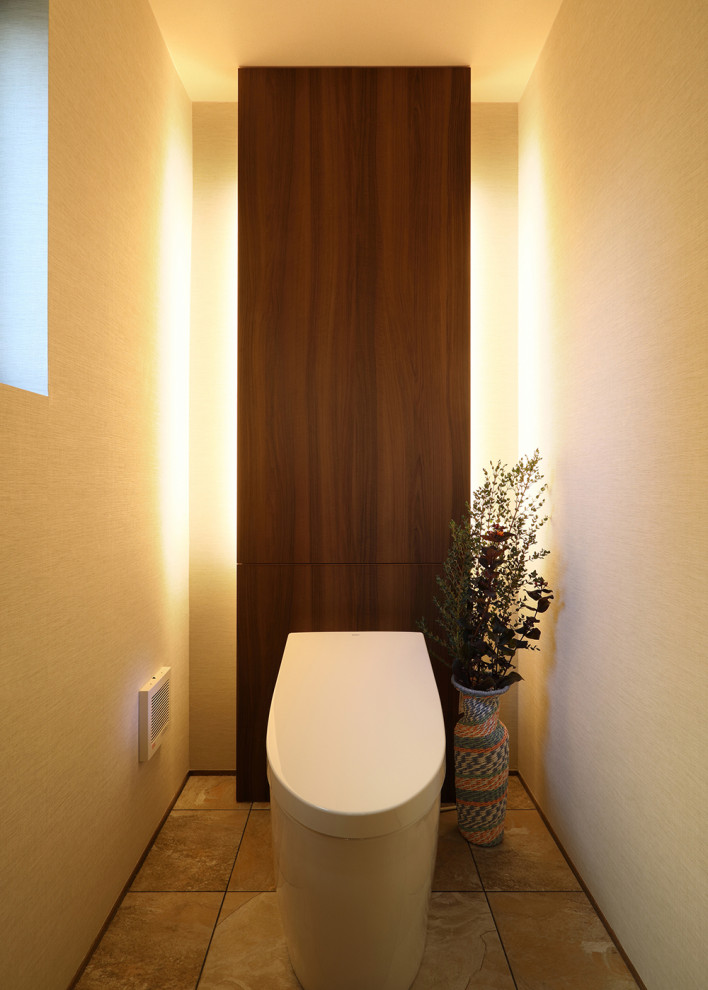 Inredning av ett mellanstort toalett, med beige väggar, brunt golv, släta luckor, en toalettstol med hel cisternkåpa, beige kakel och klinkergolv i porslin