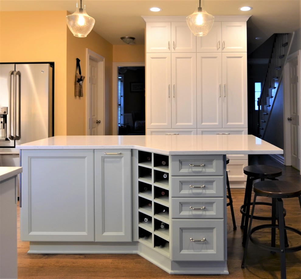 Enclosed kitchen - mid-sized transitional l-shaped medium tone wood floor and brown floor enclosed kitchen idea in Chicago with a farmhouse sink, shaker cabinets, white cabinets, quartz countertops, white backsplash, subway tile backsplash, stainless steel appliances and an island