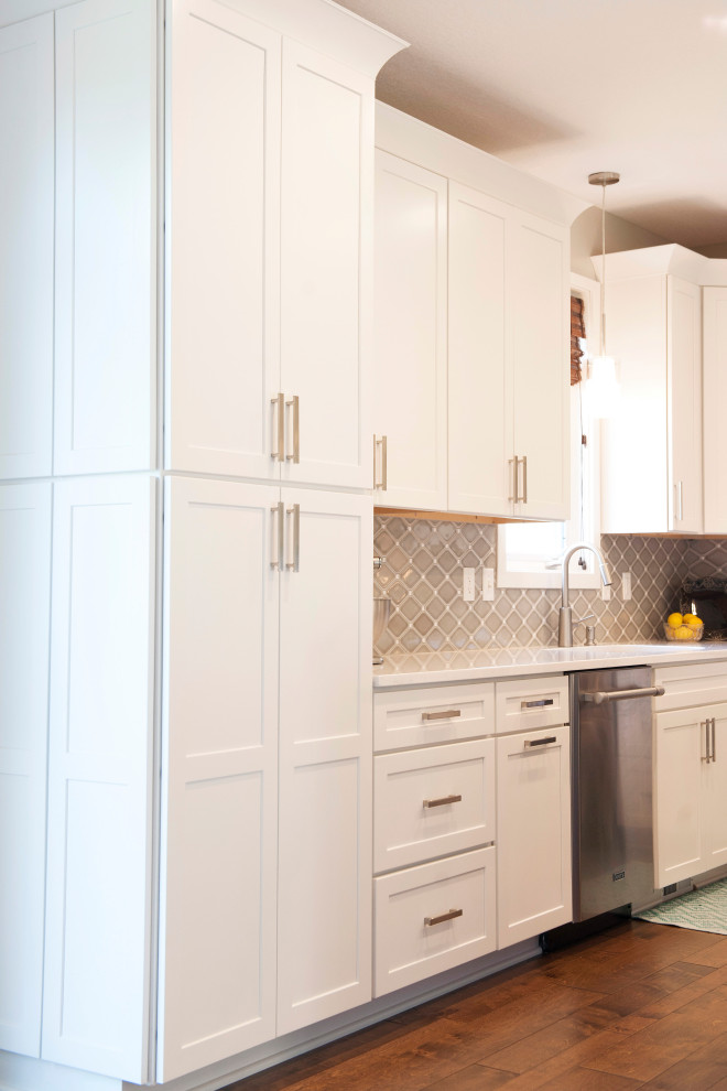 Eat-in kitchen - mid-sized transitional l-shaped medium tone wood floor and brown floor eat-in kitchen idea with an undermount sink, shaker cabinets, white cabinets, quartz countertops, gray backsplash, mosaic tile backsplash, stainless steel appliances, an island and white countertops