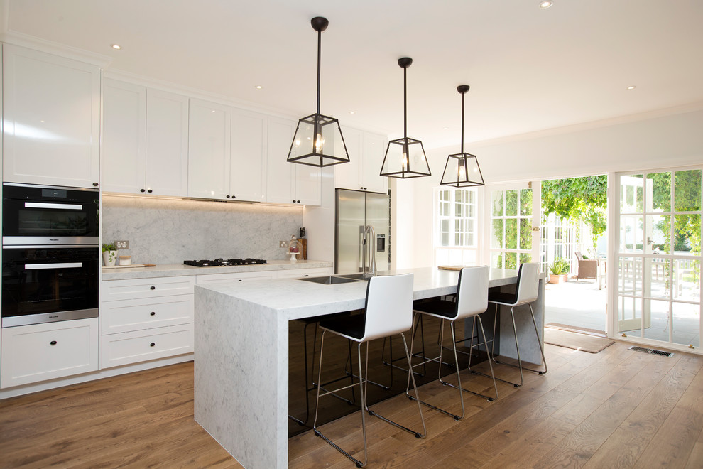 Traditional galley kitchen in Melbourne with a double-bowl sink, shaker cabinets, white cabinets, marble benchtops, marble splashback, stainless steel appliances, medium hardwood floors, brown floor, grey splashback, with island and grey benchtop.