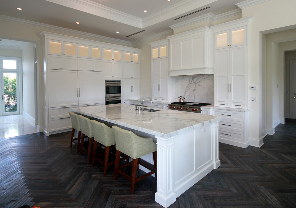 Inspiration for a mid-sized transitional l-shaped dark wood floor and brown floor enclosed kitchen remodel in Miami with an undermount sink, shaker cabinets, white cabinets, quartz countertops, white backsplash, marble backsplash, stainless steel appliances and an island