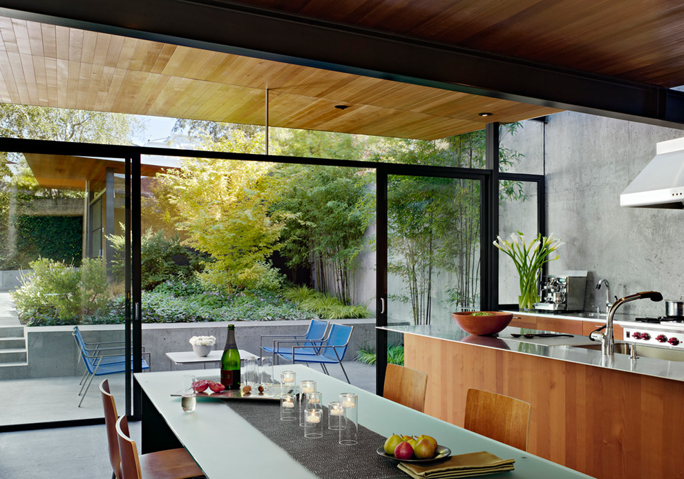 Inspiration for a mid-sized modern single-wall eat-in kitchen in San Francisco with an undermount sink, flat-panel cabinets, medium wood cabinets, stainless steel benchtops, grey splashback, stainless steel appliances, concrete floors and with island.