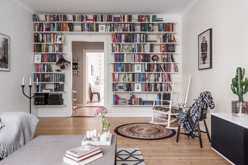 Ejemplo de sala de estar con biblioteca cerrada nórdica de tamaño medio con paredes blancas, suelo de madera clara y alfombra