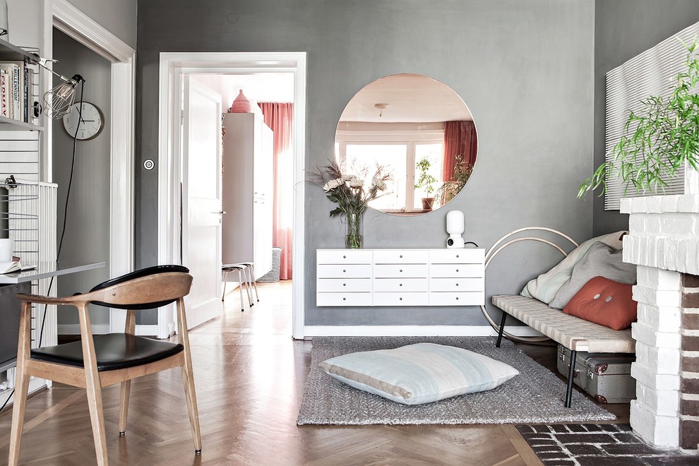 Kleines, Abgetrenntes Skandinavisches Wohnzimmer mit grauer Wandfarbe, braunem Holzboden, Kamin, Kaminumrandung aus Backstein und braunem Boden in Malmö