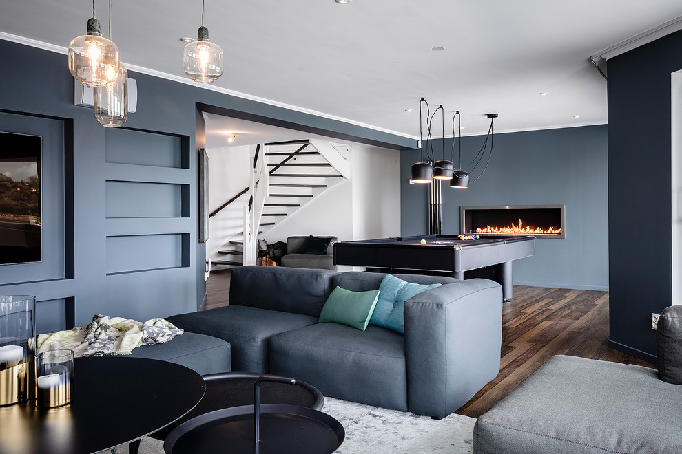 Ejemplo de sala de estar cerrada escandinava grande con paredes azules, suelo de madera oscura, suelo marrón, chimenea lineal y televisor colgado en la pared