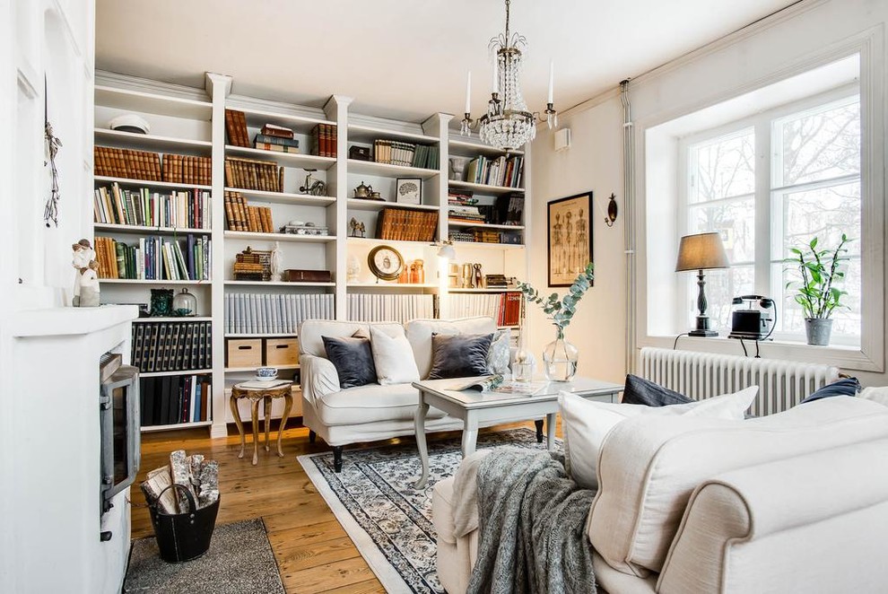 Foto på ett litet skandinaviskt separat vardagsrum, med ett bibliotek, vita väggar, mellanmörkt trägolv, en öppen vedspis, en spiselkrans i gips och brunt golv