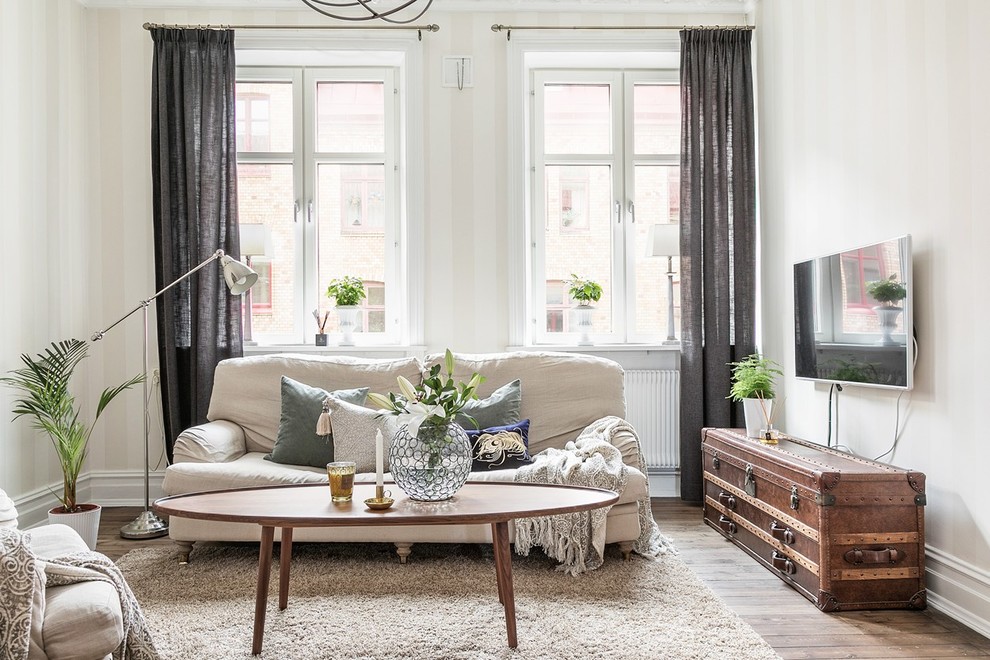 На фото: гостиная комната в скандинавском стиле с белыми стенами, паркетным полом среднего тона, телевизором на стене и коричневым полом