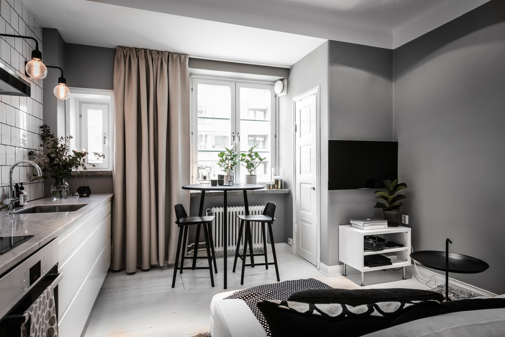 На фото: маленькая открытая гостиная комната в скандинавском стиле с серыми стенами, деревянным полом, телевизором на стене и белым полом для на участке и в саду с
