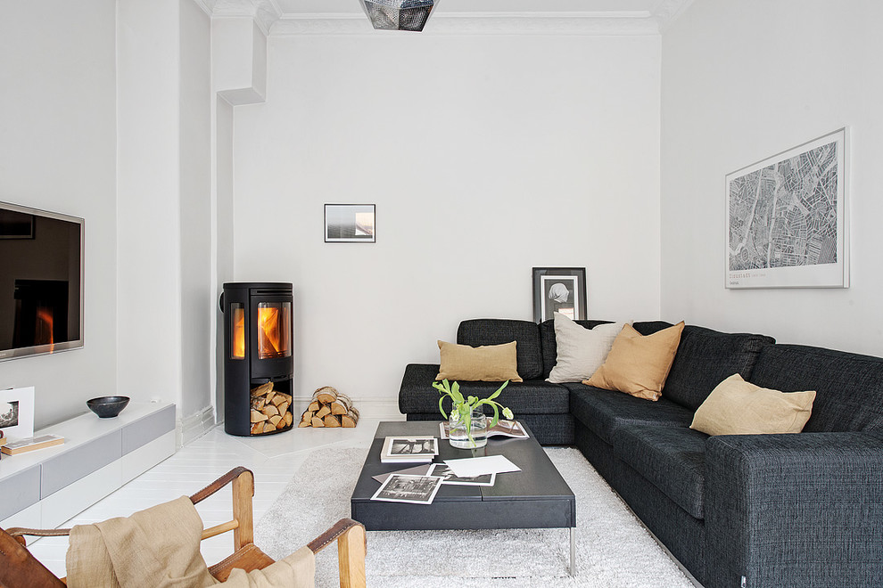 Diseño de sala de estar abierta escandinava de tamaño medio con paredes blancas, suelo de madera pintada, televisor colgado en la pared y estufa de leña