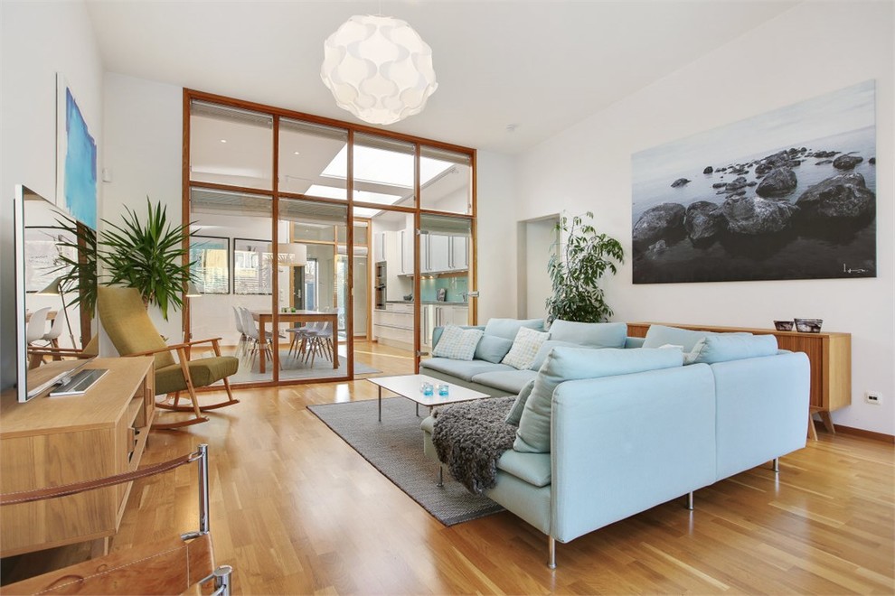 Modelo de sala de estar abierta escandinava grande sin chimenea y televisor con paredes blancas y suelo de madera en tonos medios