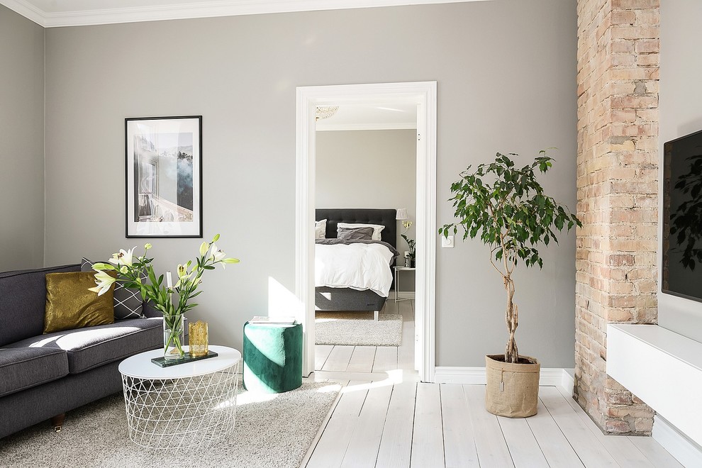 На фото: гостиная комната в скандинавском стиле с серыми стенами, деревянным полом, телевизором на стене и белым полом