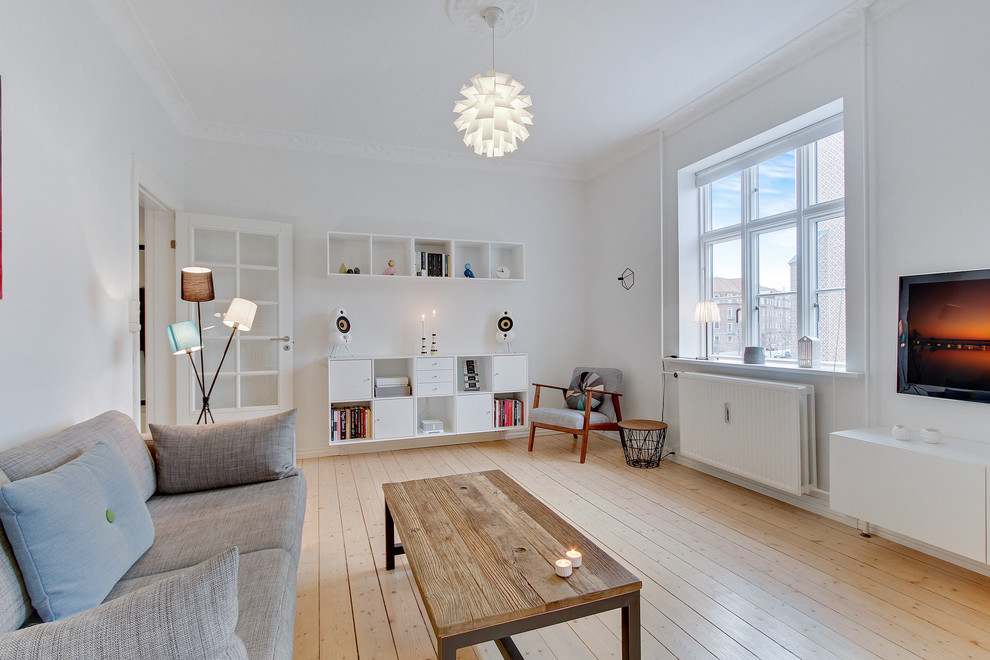 Immagine di un soggiorno scandinavo chiuso e di medie dimensioni con pareti bianche, parquet chiaro, TV a parete e nessun camino