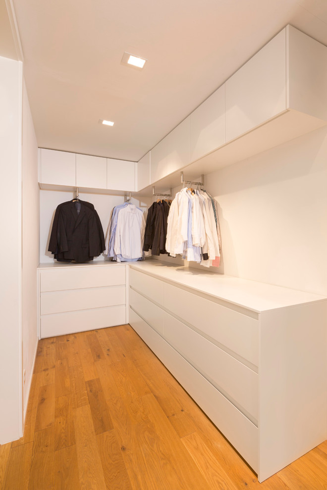 Immagine di una piccola cabina armadio per uomo moderna con pavimento in legno massello medio, ante lisce e ante bianche