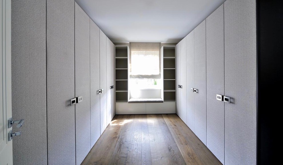 Inspiration pour un grand dressing minimaliste neutre avec des portes de placard blanches, un placard à porte plane, parquet foncé et un sol marron.