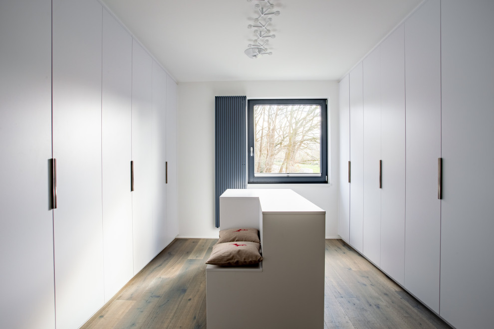 Neutraler, Großer Moderner Begehbarer Kleiderschrank mit flächenbündigen Schrankfronten, weißen Schränken, dunklem Holzboden und braunem Boden in Dortmund