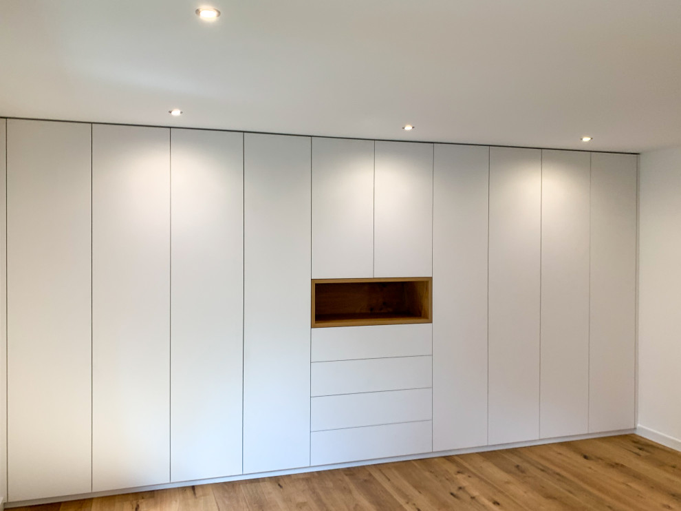 Immagine di un grande spazio per vestirsi minimal con ante lisce, ante bianche, pavimento in legno massello medio e pavimento marrone