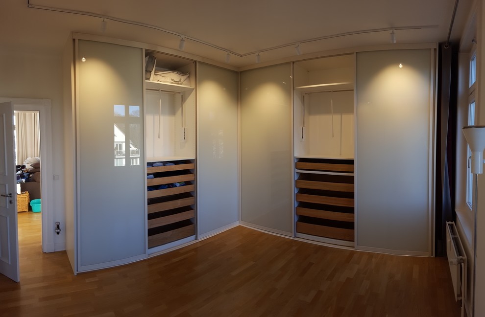 Ejemplo de armario unisex actual de tamaño medio con armarios con paneles lisos, puertas de armario blancas, suelo laminado y suelo marrón
