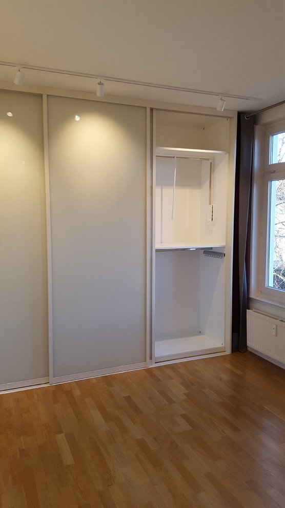 Esempio di un armadio o armadio a muro unisex design di medie dimensioni con ante lisce, ante bianche, pavimento in laminato e pavimento marrone