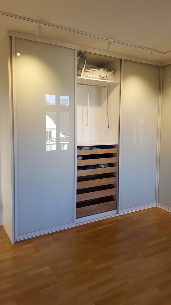 Diseño de armario unisex actual de tamaño medio con armarios con paneles lisos, puertas de armario blancas, suelo laminado y suelo marrón
