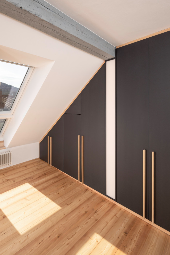 Foto di una cabina armadio unisex minimalista di medie dimensioni con ante lisce, ante nere, parquet chiaro, pavimento marrone e travi a vista