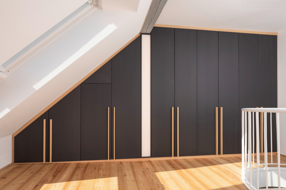 Inspiration för mellanstora moderna walk-in-closets för könsneutrala, med släta luckor, svarta skåp, ljust trägolv och brunt golv