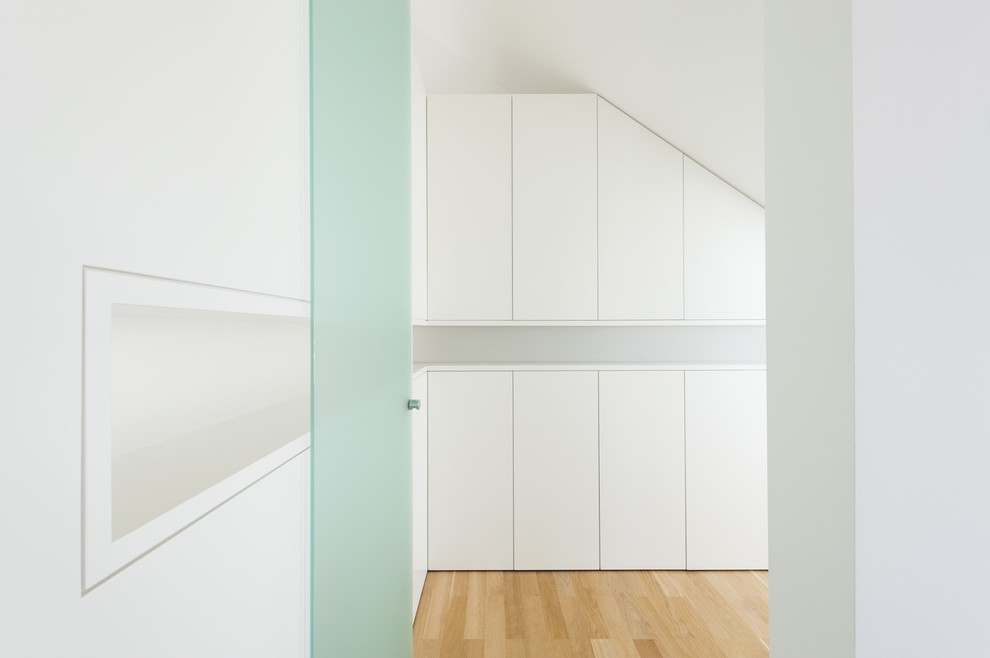 Immagine di uno spazio per vestirsi unisex minimalista con ante lisce, ante bianche e parquet chiaro