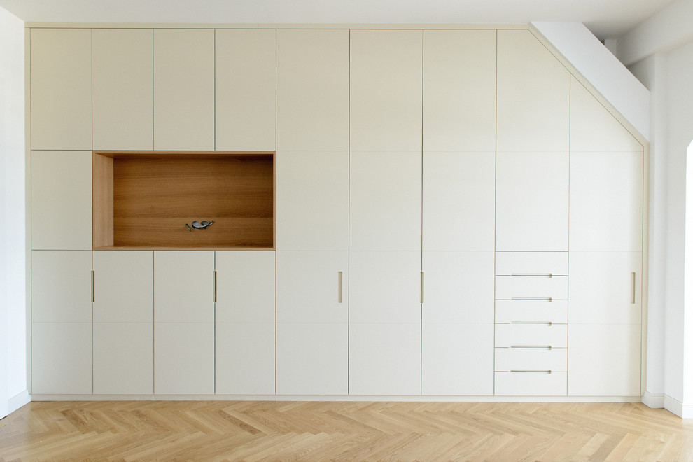 Ejemplo de vestidor unisex actual extra grande con armarios con paneles lisos, puertas de armario beige, suelo de madera clara y suelo beige