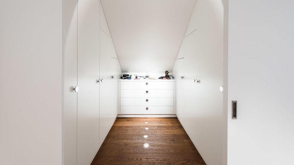 Inspiration for a small contemporary gender-neutral medium tone wood floor and brown floor walk-in closet remodel in Other with flat-panel cabinets and white cabinets