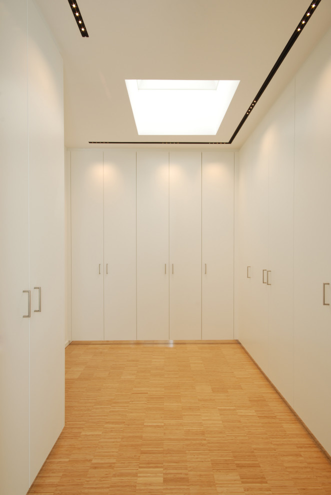 Idées déco pour un placard dressing moderne de taille moyenne avec un placard à porte plane, des portes de placard blanches, parquet en bambou et un sol beige.