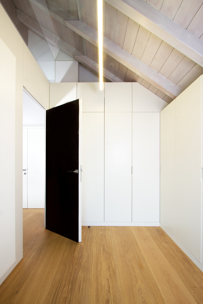 На фото: гардеробная комната унисекс в стиле модернизм с плоскими фасадами, белыми фасадами и паркетным полом среднего тона