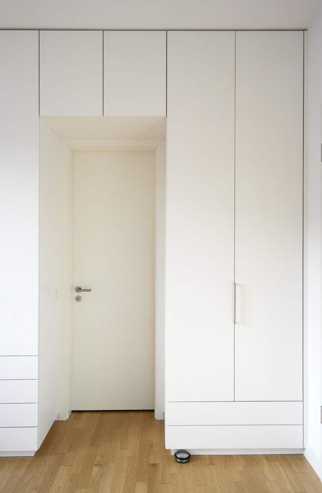 Photo of a modern standard wardrobe in Berlin with flat-panel cabinets, white cabinets and medium hardwood flooring.