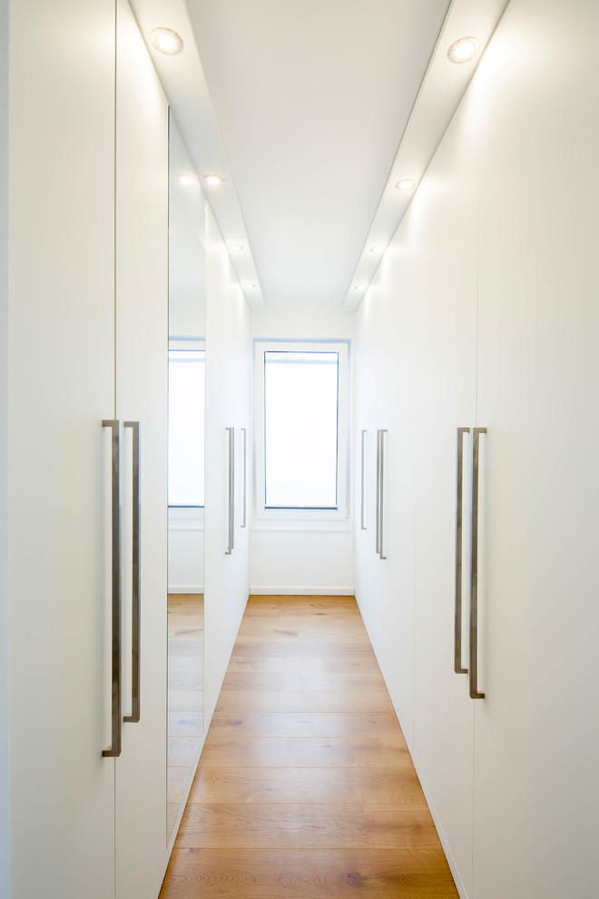 Mittelgroßer Moderner Begehbarer Kleiderschrank mit flächenbündigen Schrankfronten, weißen Schränken und braunem Holzboden in Düsseldorf