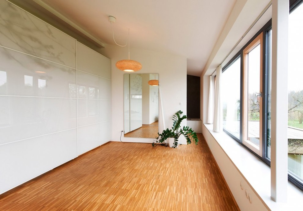 Cette photo montre un grand dressing room tendance neutre avec des portes de placard blanches, un sol en bois brun et un sol marron.