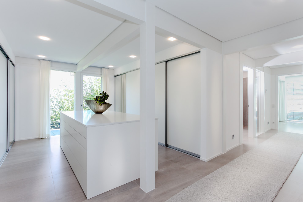 Inspiration for a large contemporary gender neutral walk-in wardrobe in Other with flat-panel cabinets, white cabinets, ceramic flooring and beige floors.