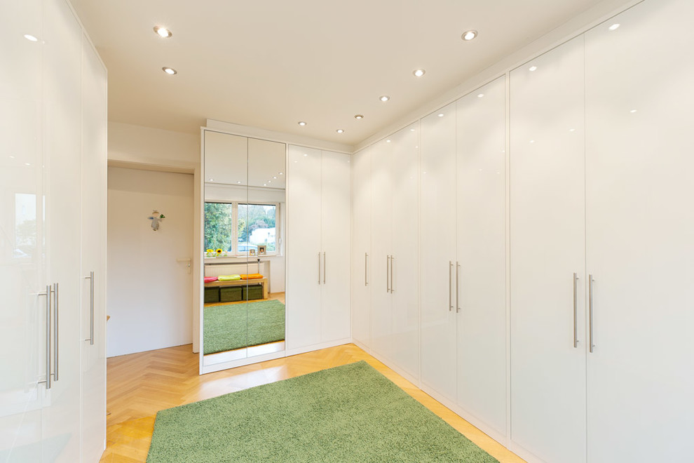 Inspiration for a large contemporary gender neutral walk-in wardrobe in Essen with flat-panel cabinets, white cabinets and light hardwood flooring.