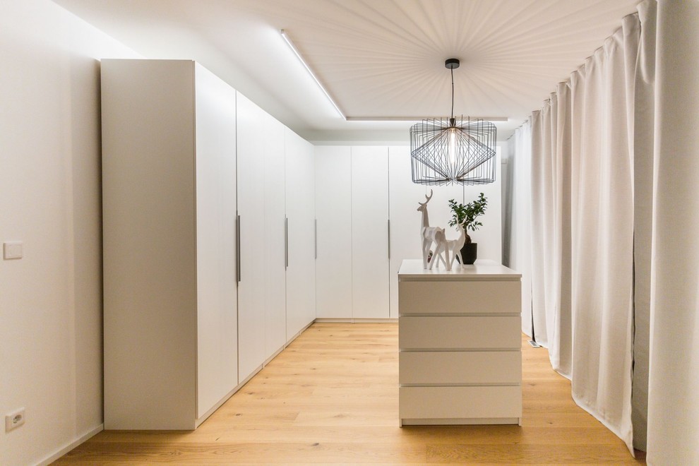 Geräumiger, Neutraler Moderner Begehbarer Kleiderschrank mit flächenbündigen Schrankfronten, weißen Schränken, hellem Holzboden und braunem Boden in Dortmund
