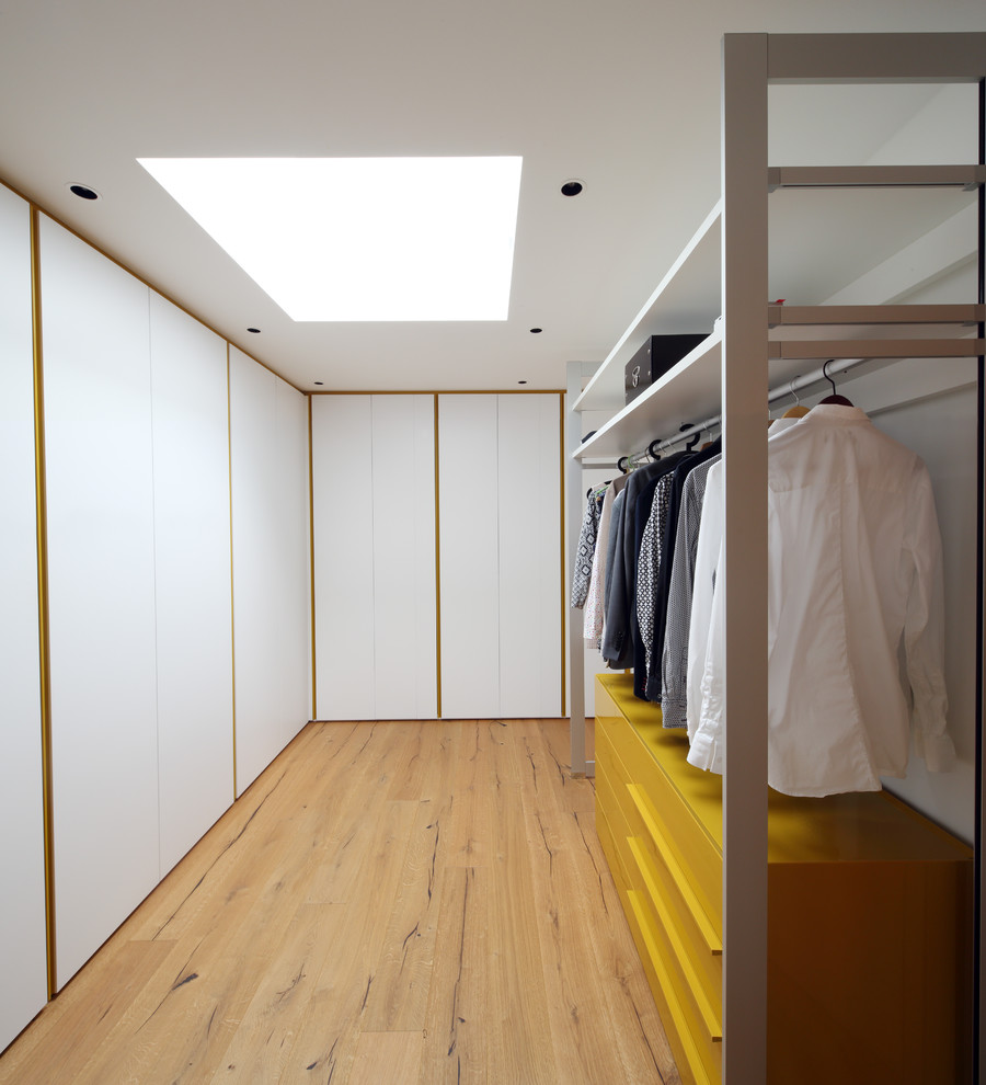 Foto de armario vestidor unisex actual grande con armarios con paneles lisos, puertas de armario blancas y suelo de madera clara
