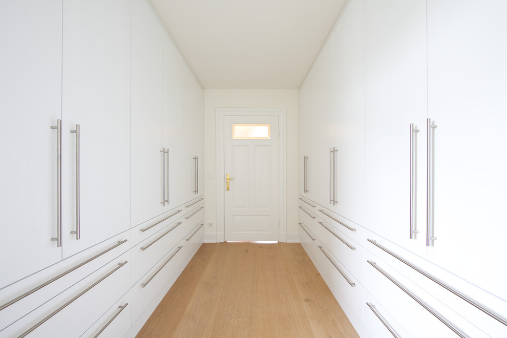 Exemple d'un grand dressing room chic neutre avec un placard à porte plane, des portes de placard blanches et parquet clair.