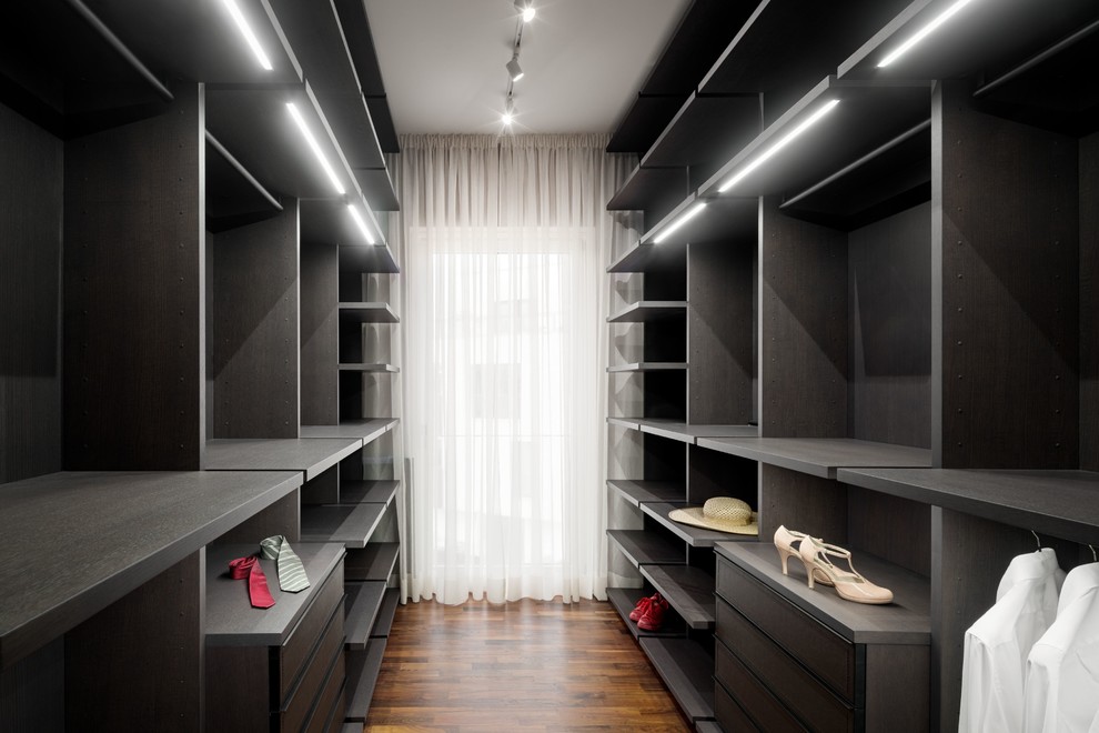 Large contemporary gender neutral walk-in wardrobe in Berlin with open cabinets, dark wood cabinets, medium hardwood flooring and brown floors.