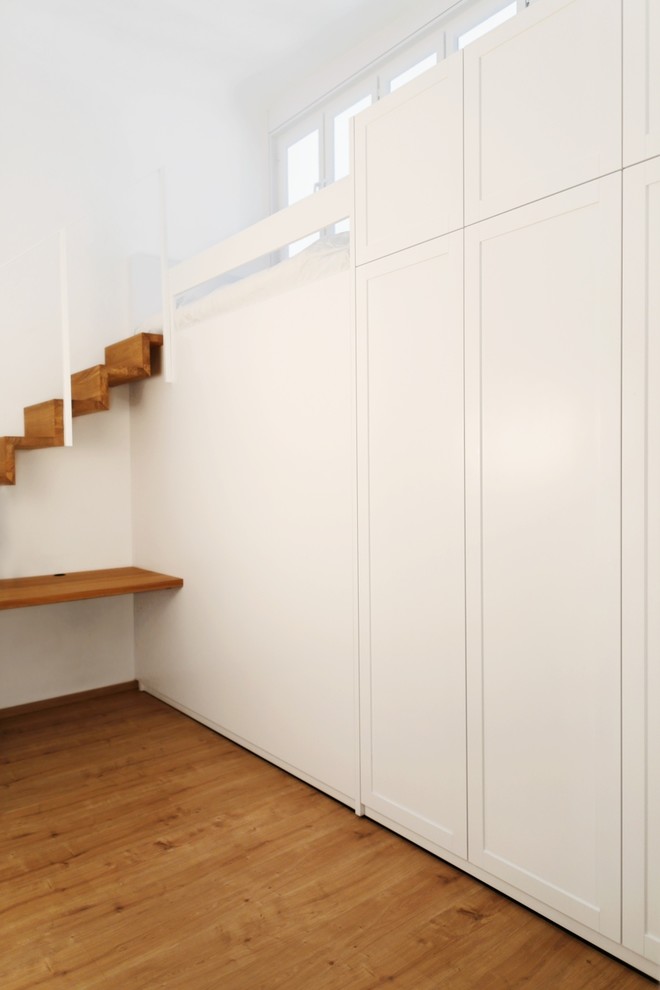 Ispirazione per un piccolo armadio o armadio a muro minimalista con ante con bugna sagomata, ante bianche, parquet chiaro e pavimento marrone