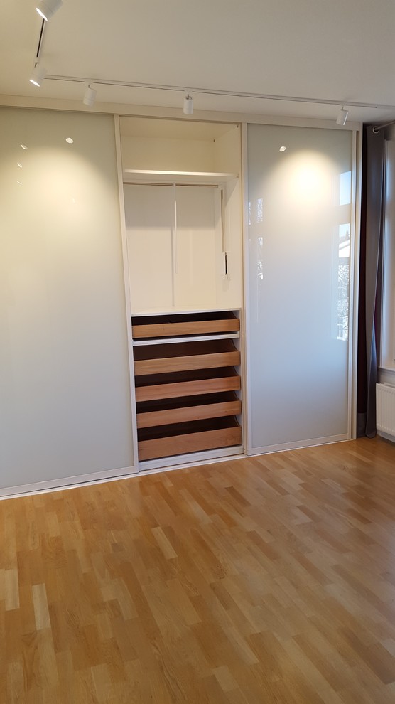 Diseño de armario unisex contemporáneo de tamaño medio con armarios con paneles lisos, puertas de armario blancas, suelo laminado y suelo marrón