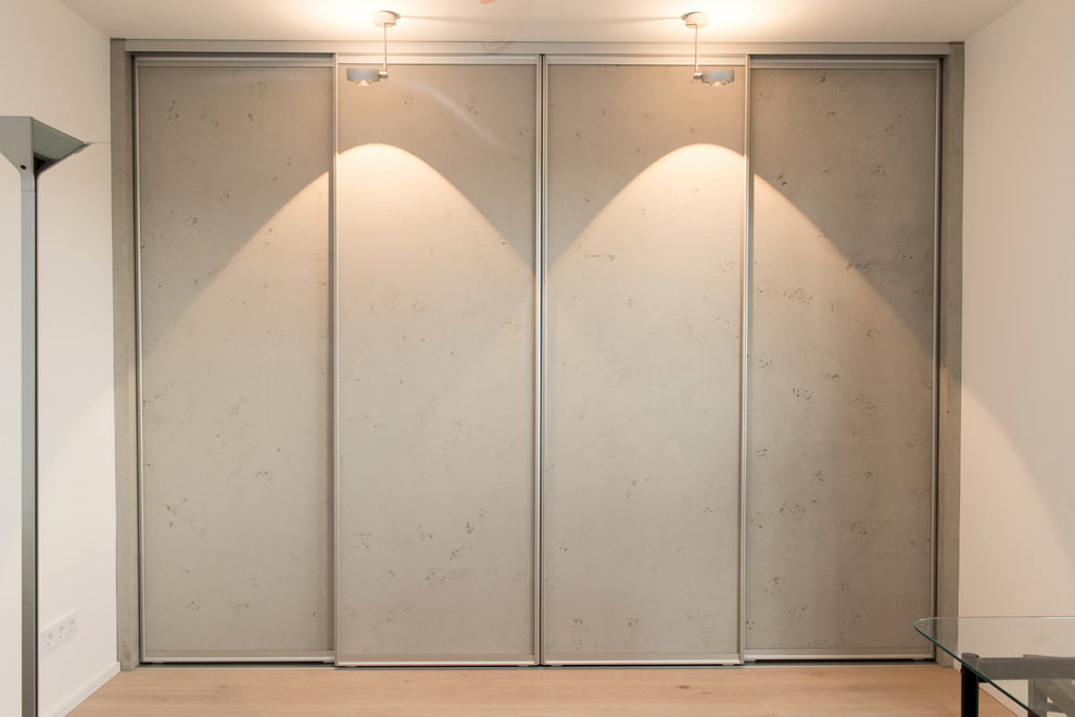 Geräumiges, Neutrales Modernes Ankleidezimmer mit Ankleidebereich, flächenbündigen Schrankfronten, grauen Schränken, hellem Holzboden und braunem Boden in München